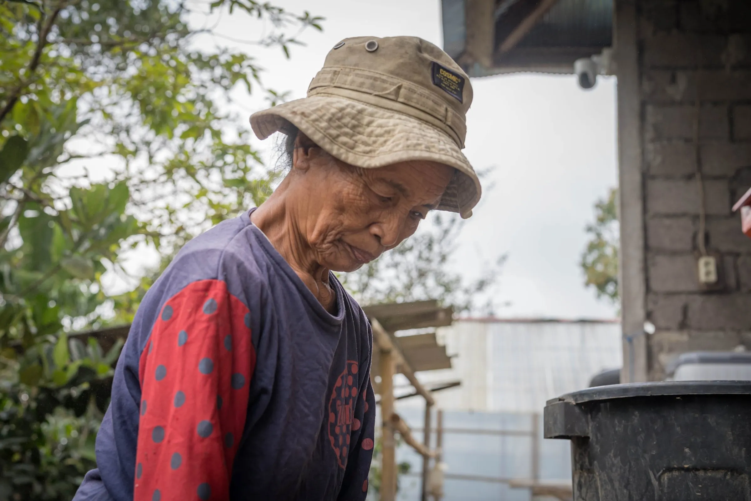 Ibu Ketut in a bucket hat looking down at coffee in her hands