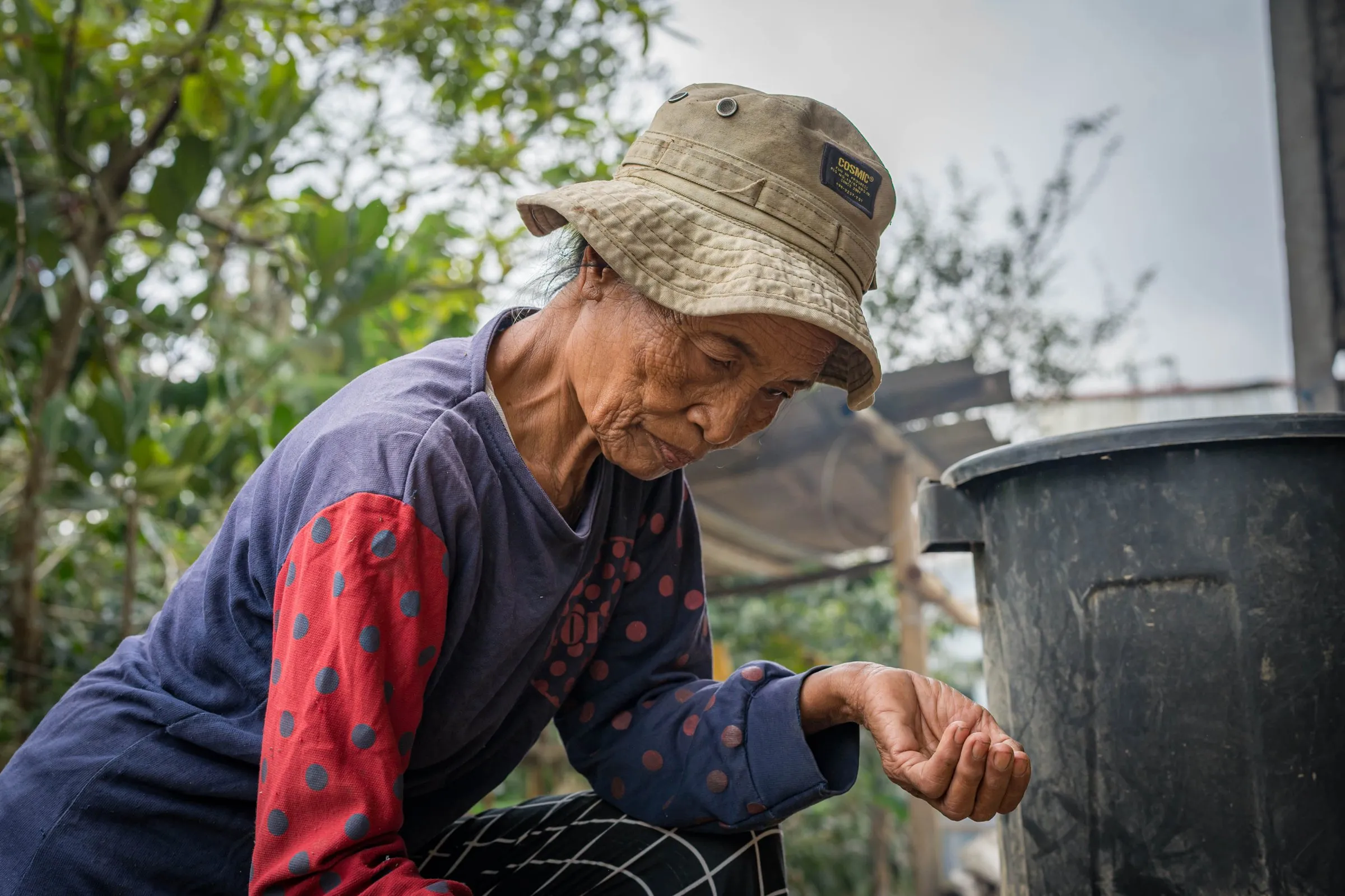 Ibu Ketut crouching over a bucket, sorting coffee in her palm