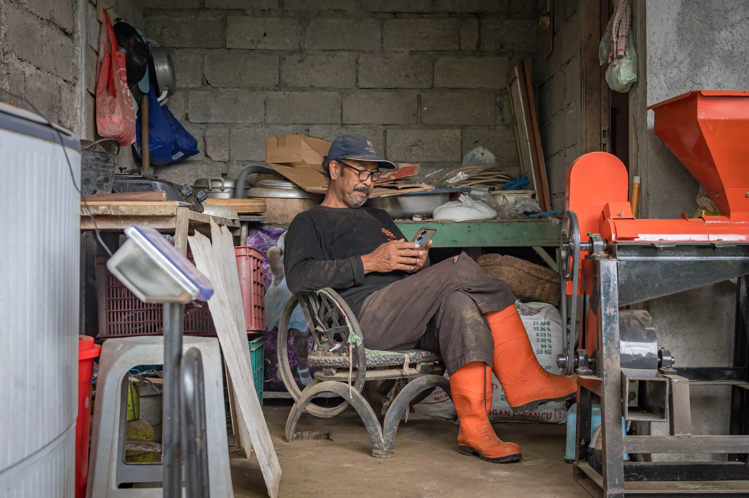A man in orange boots sitting in the workshop next to the red huller
